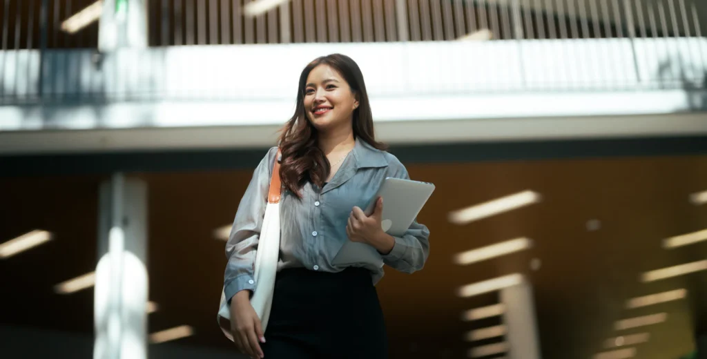 Young Asian woman student smiling, walking confidently, holding a laptop and carry bag